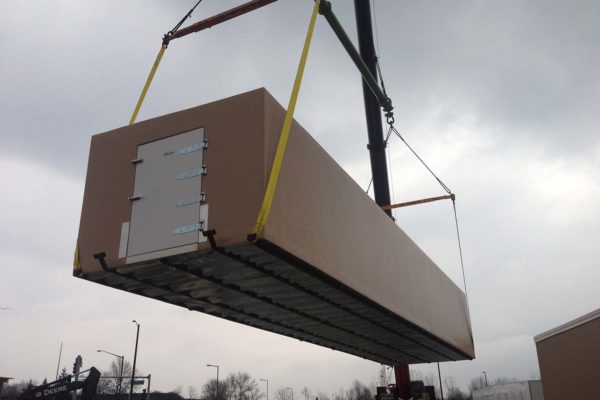 Crane lifting a tan colored walk in freezer for delivery